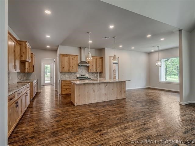 kitchen featuring a wealth of natural light, a kitchen island with sink, wall chimney exhaust hood, and pendant lighting