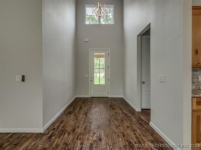 entryway with a towering ceiling, dark hardwood / wood-style floors, plenty of natural light, and a notable chandelier