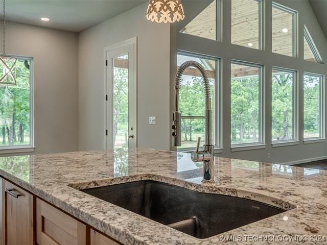 kitchen with light stone counters, sink, decorative light fixtures, and light brown cabinets