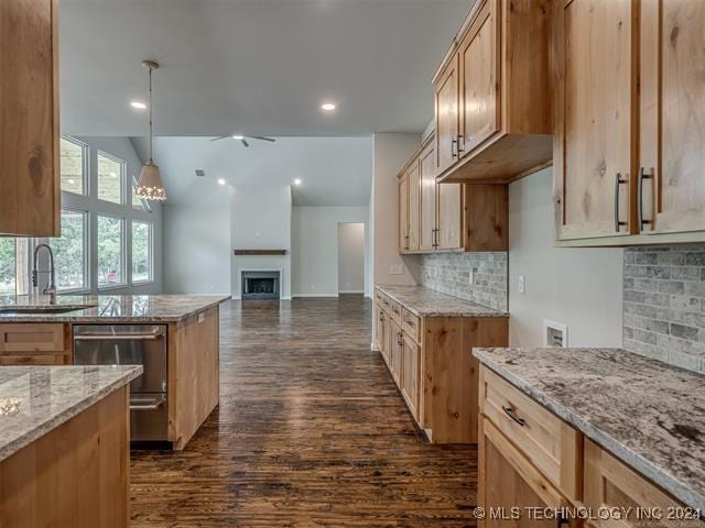 kitchen featuring light stone countertops, dishwasher, sink, backsplash, and pendant lighting