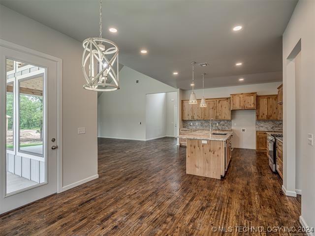 kitchen with decorative light fixtures, an island with sink, stainless steel range, and tasteful backsplash