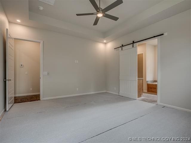 unfurnished bedroom with light carpet, a raised ceiling, ensuite bath, ceiling fan, and a barn door