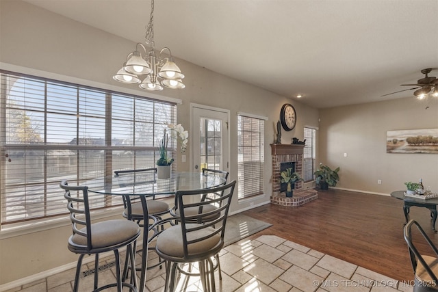 dining area with ceiling fan with notable chandelier, light wood-type flooring, and a brick fireplace