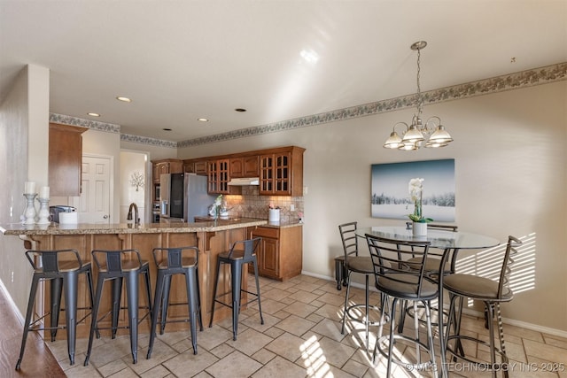 kitchen featuring decorative backsplash, stainless steel fridge, kitchen peninsula, pendant lighting, and a notable chandelier