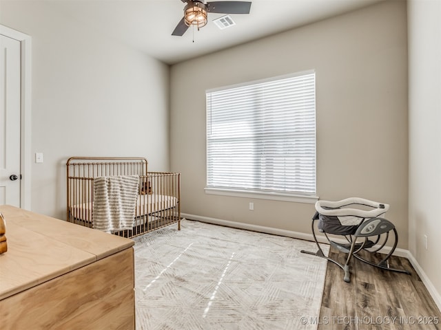 bedroom with a nursery area, ceiling fan, and light hardwood / wood-style flooring