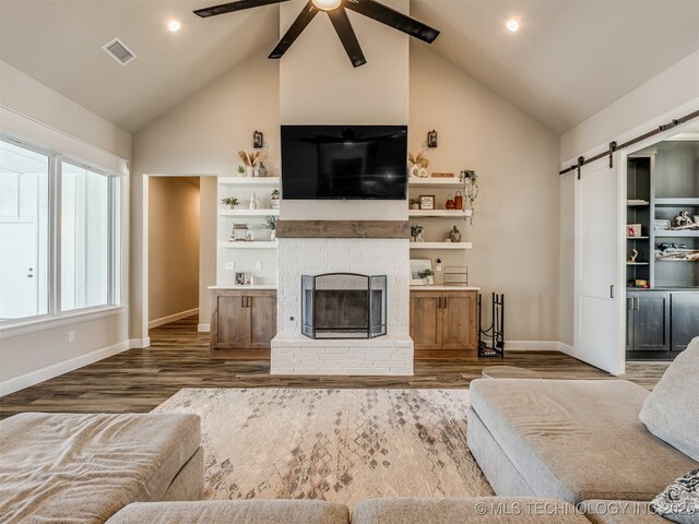 living room with ceiling fan, a barn door, a fireplace, and hardwood / wood-style flooring