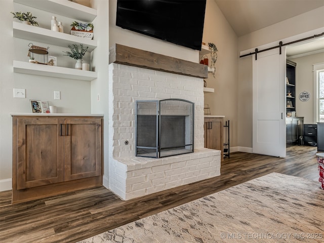 living room featuring lofted ceiling, a fireplace, a barn door, and dark wood-type flooring