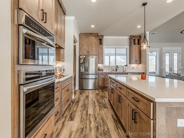 kitchen with hanging light fixtures, stainless steel appliances, hardwood / wood-style floors, a kitchen island, and sink