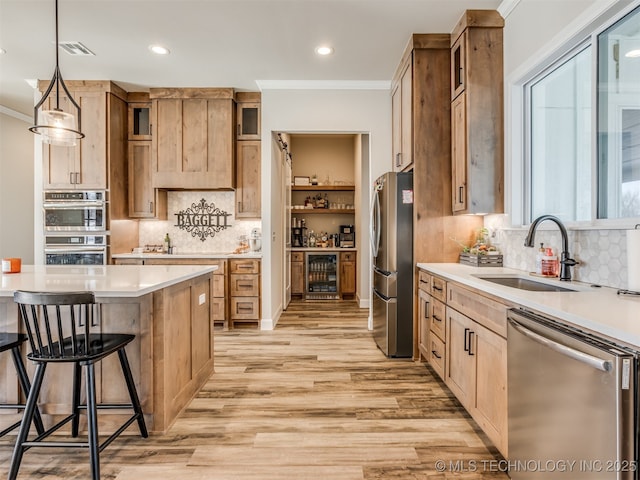 kitchen with sink, ornamental molding, light hardwood / wood-style flooring, hanging light fixtures, and appliances with stainless steel finishes