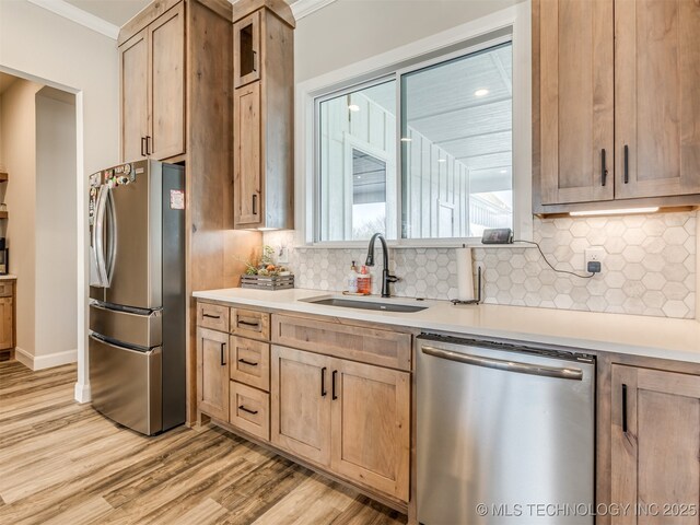 kitchen featuring stainless steel appliances, light wood-type flooring, ornamental molding, and sink