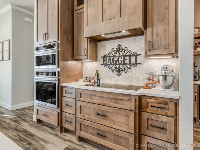 kitchen featuring hardwood / wood-style flooring, exhaust hood, black electric cooktop, crown molding, and double oven