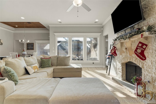 living room featuring a stone fireplace, light hardwood / wood-style flooring, ceiling fan with notable chandelier, and ornamental molding