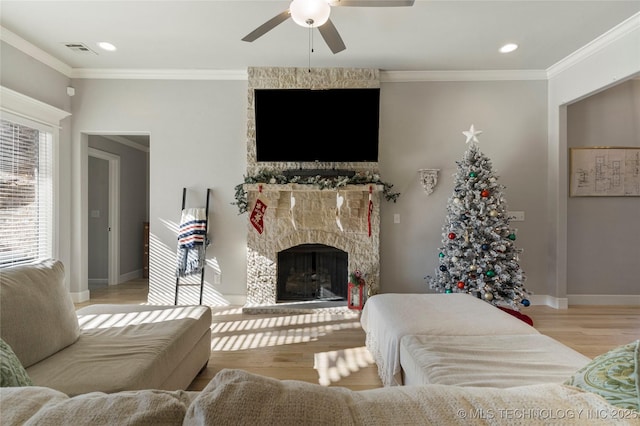 living room with a stone fireplace, ceiling fan, light hardwood / wood-style floors, and ornamental molding