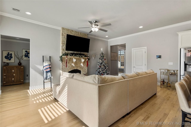 living room featuring light wood-type flooring, a stone fireplace, ceiling fan, and crown molding