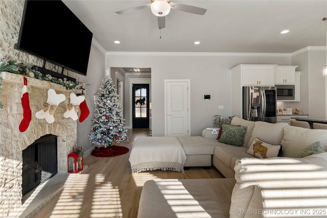 living room featuring crown molding, a fireplace, ceiling fan, and light hardwood / wood-style flooring