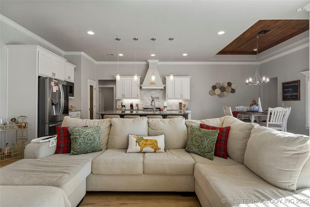 living room featuring sink, light hardwood / wood-style floors, a notable chandelier, and ornamental molding