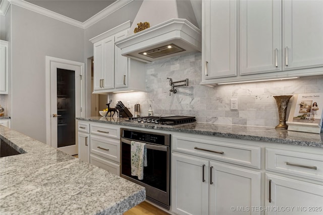 kitchen featuring appliances with stainless steel finishes, backsplash, premium range hood, crown molding, and white cabinets