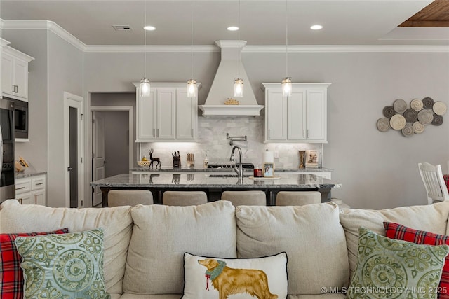 kitchen with a center island with sink, white cabinetry, light stone countertops, and hanging light fixtures