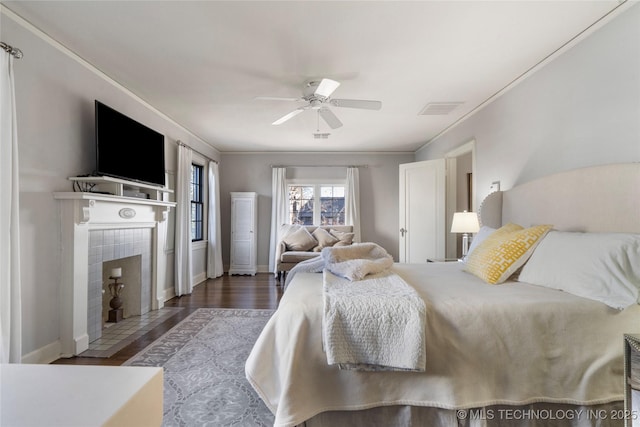 bedroom with a tile fireplace, ceiling fan, crown molding, and dark hardwood / wood-style floors