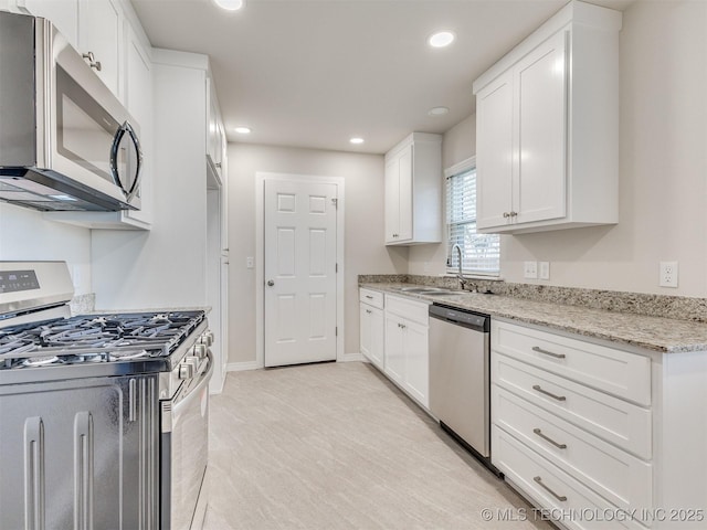 kitchen with light stone counters, sink, appliances with stainless steel finishes, and white cabinetry