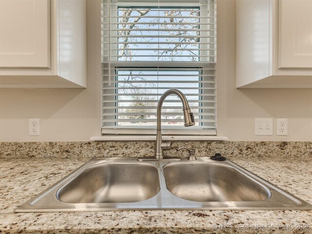 interior details with sink, white cabinetry, and light stone counters