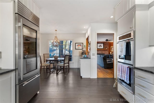 kitchen featuring appliances with stainless steel finishes, pendant lighting, white cabinetry, dark hardwood / wood-style flooring, and a brick fireplace