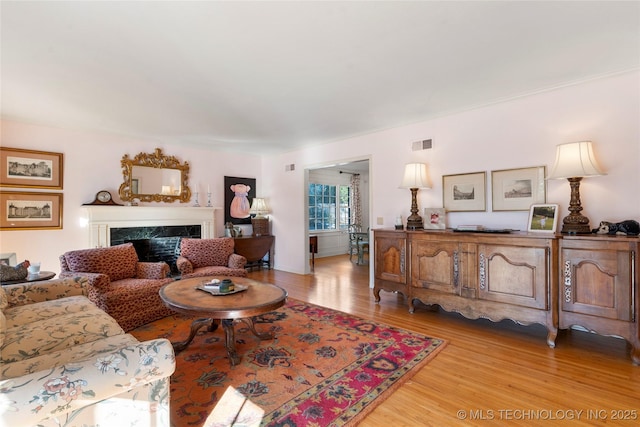 living room with a high end fireplace and light hardwood / wood-style floors