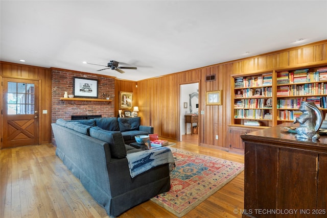 living room featuring a brick fireplace, wood walls, and light wood-type flooring