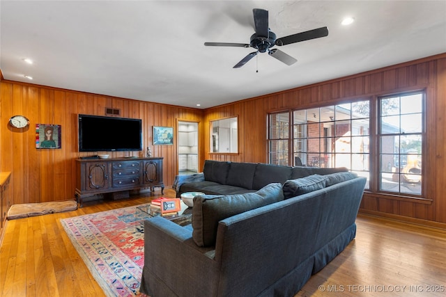 living room with light hardwood / wood-style flooring, ceiling fan, and wood walls