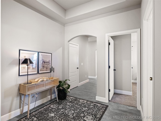 hall with arched walkways, baseboards, and wood finished floors