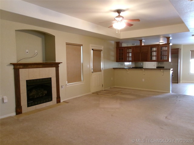 unfurnished living room with a tile fireplace, ceiling fan, and light colored carpet