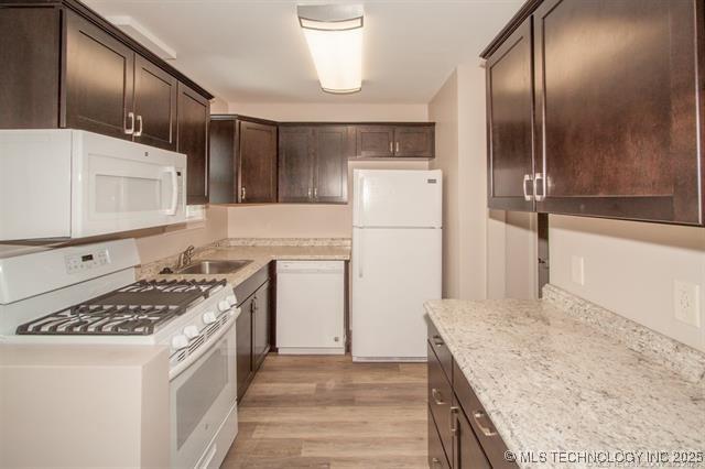 kitchen featuring light stone countertops, white appliances, dark brown cabinetry, sink, and light hardwood / wood-style flooring