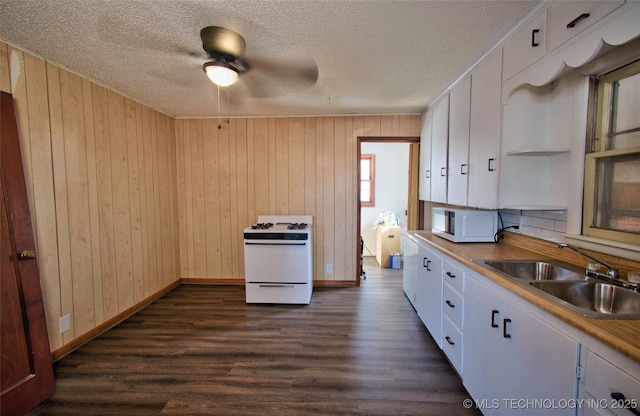 kitchen with wooden walls, sink, white cabinets, and white appliances