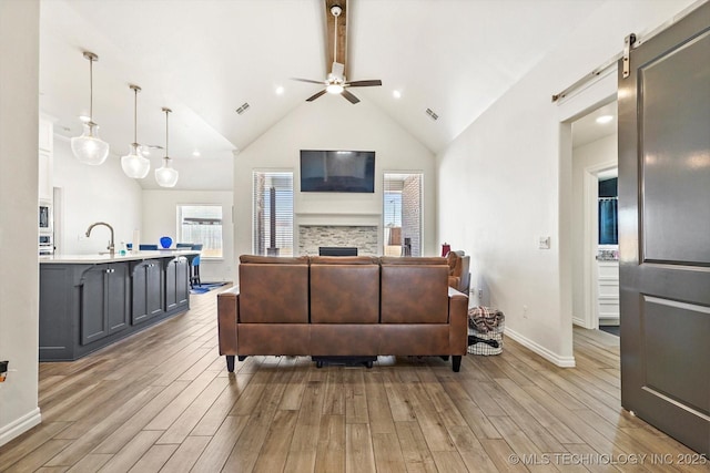 living room featuring light hardwood / wood-style floors, lofted ceiling, a barn door, ceiling fan, and sink