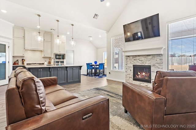 living room featuring lofted ceiling, light hardwood / wood-style flooring, and a stone fireplace