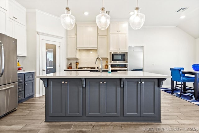 kitchen featuring hanging light fixtures, a center island with sink, tasteful backsplash, white cabinets, and appliances with stainless steel finishes