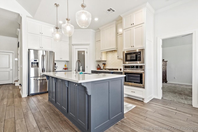 kitchen featuring pendant lighting, a center island with sink, backsplash, white cabinets, and appliances with stainless steel finishes