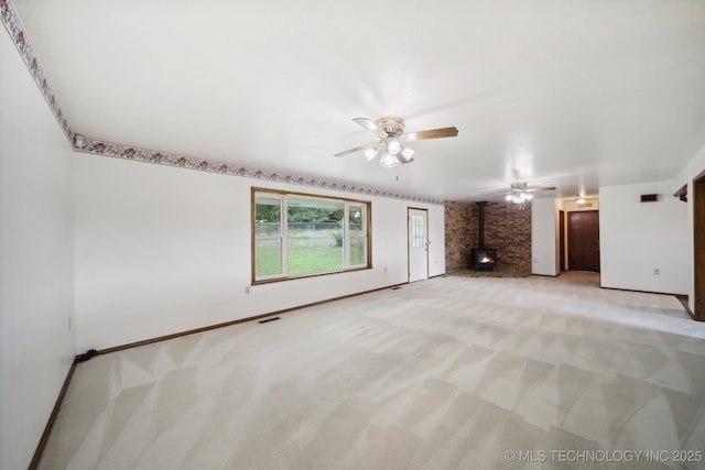 unfurnished living room with ceiling fan, a wood stove, and light colored carpet