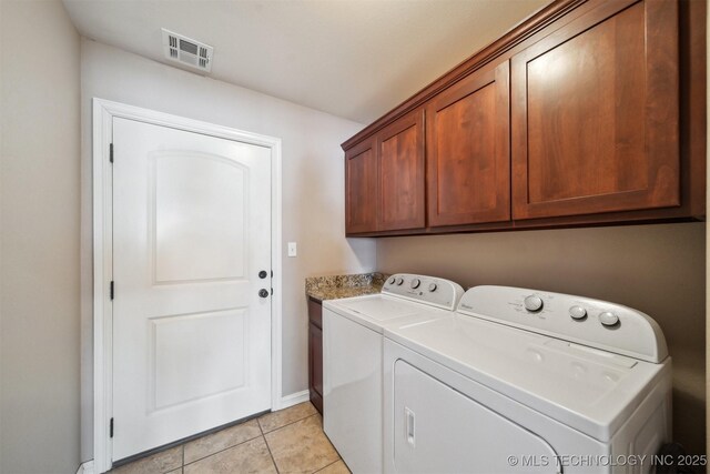 clothes washing area with cabinets, washing machine and clothes dryer, and light tile patterned floors