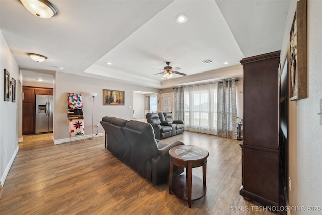 living room with a raised ceiling, ceiling fan, and light hardwood / wood-style floors