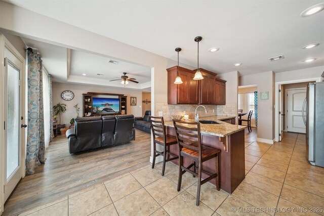 kitchen with stainless steel refrigerator, kitchen peninsula, a breakfast bar, a tray ceiling, and decorative light fixtures