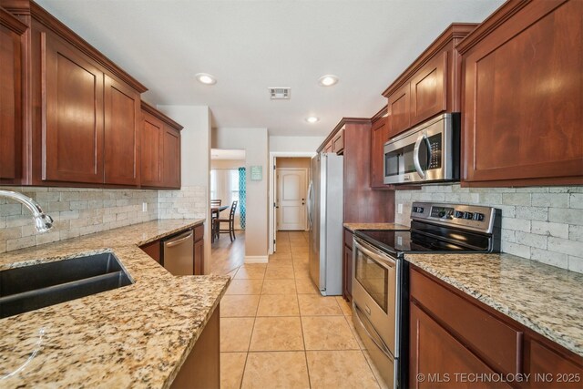 kitchen with light stone counters, light tile patterned floors, backsplash, appliances with stainless steel finishes, and sink