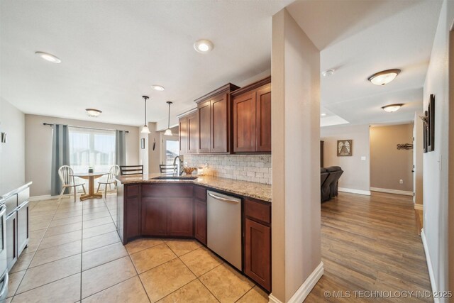 kitchen featuring sink, decorative light fixtures, dishwasher, backsplash, and light stone countertops