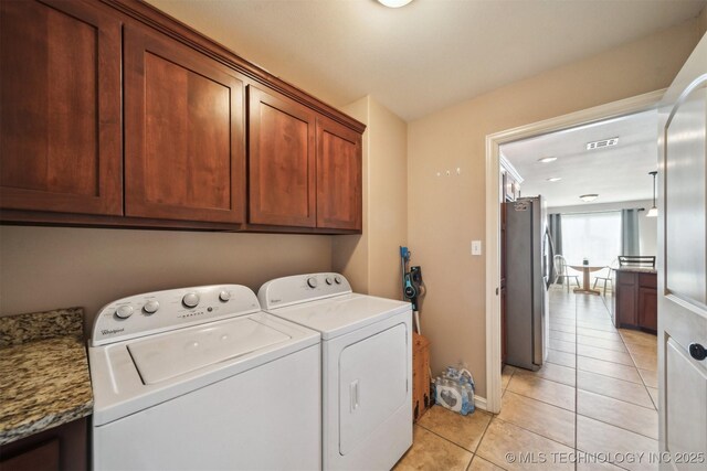 clothes washing area with washer and dryer, light tile patterned floors, and cabinets