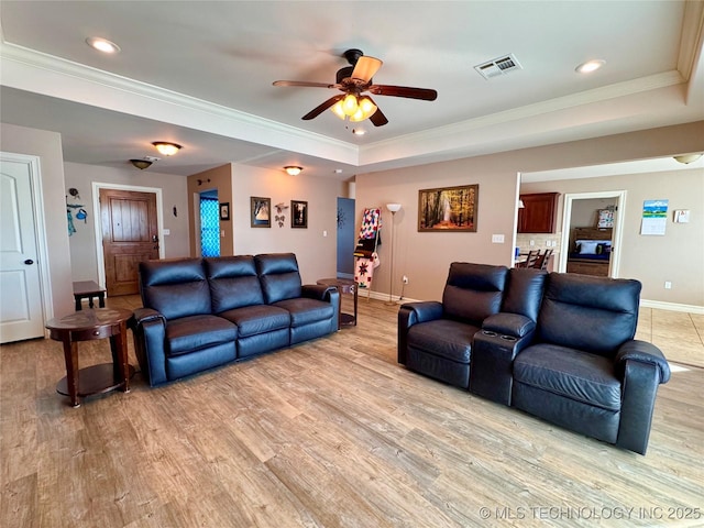 living room with light wood-type flooring, ceiling fan, ornamental molding, and a tray ceiling