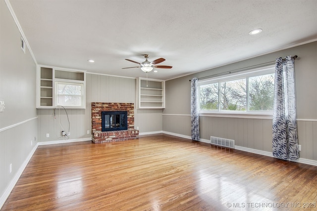 unfurnished living room featuring wood-type flooring, a brick fireplace, ceiling fan, and built in shelves