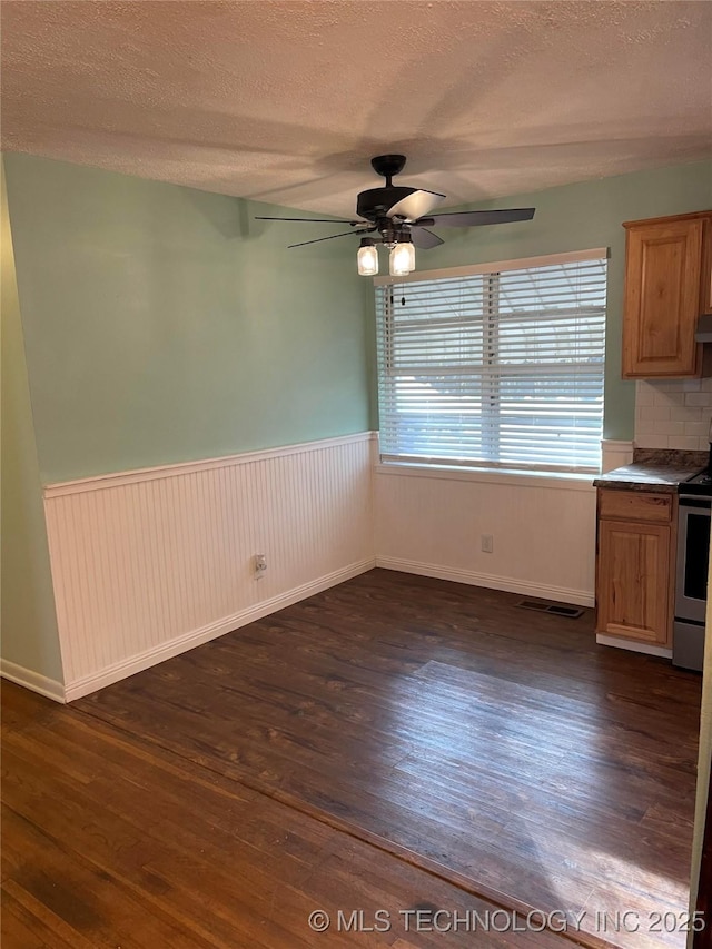 unfurnished dining area with ceiling fan, a textured ceiling, and dark hardwood / wood-style floors