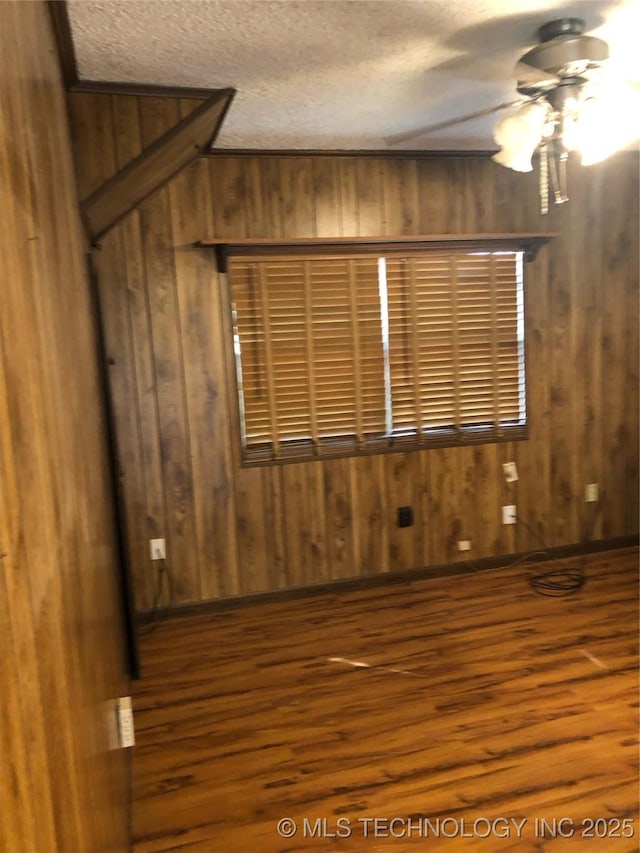 empty room with wood walls, ceiling fan, a textured ceiling, and dark hardwood / wood-style floors