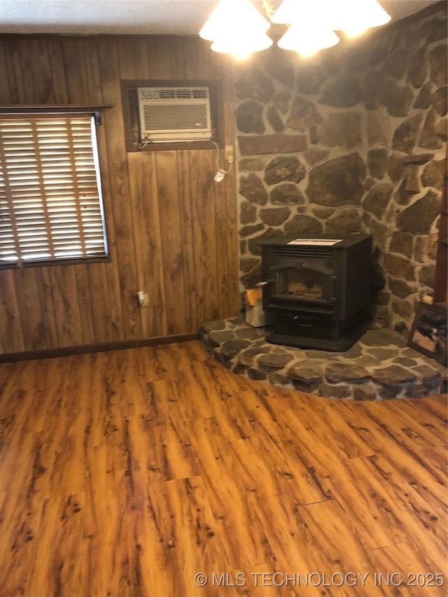 unfurnished living room featuring hardwood / wood-style flooring, a wall mounted AC, wooden walls, and a wood stove