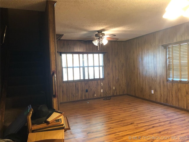 empty room featuring ceiling fan, wood walls, a textured ceiling, and hardwood / wood-style flooring